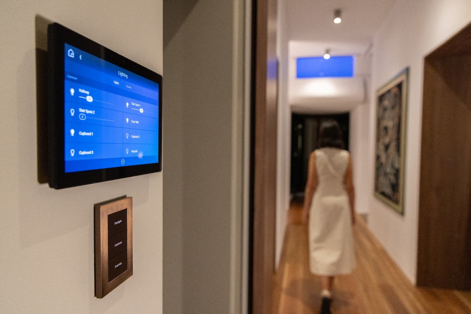 Home-control touchscreen and scene keypad beside a warmly lit residential hallway