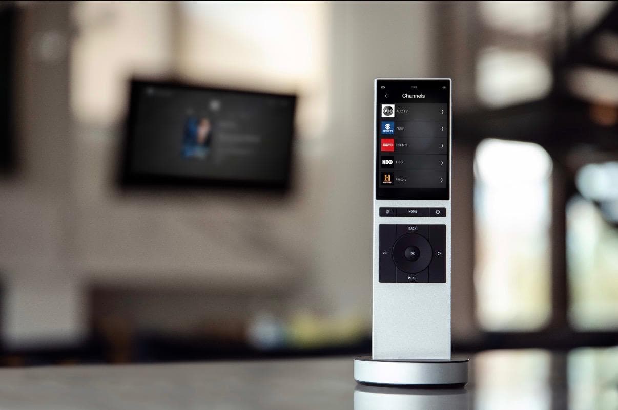 Handheld media controller on a charging base with a television in the background